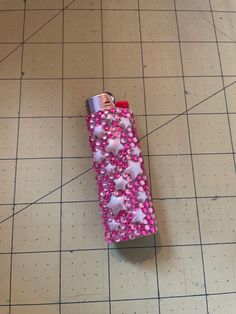 a lighter with pink and white hearts on it sitting on a tile floor next to a ruler