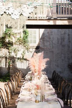 a long table is set with white linens and tall pink pamolite centerpieces