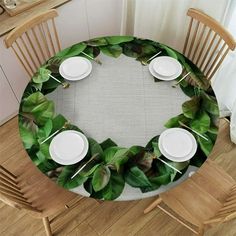 the table is set with white plates and green leaves on it, along with two wooden chairs