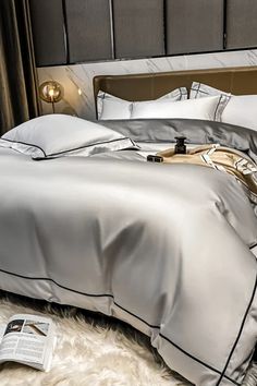 a bed with silver sheets and pillows on top of a fluffy white carpeted floor