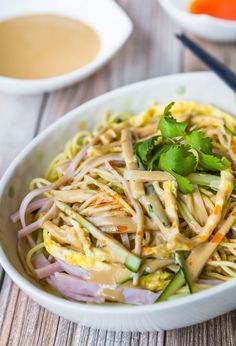 a white bowl filled with noodles and veggies next to some chopsticks