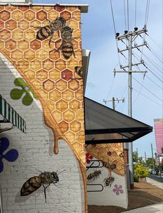 the mural on the side of a building depicts bees and honeycombs, with power lines in the background