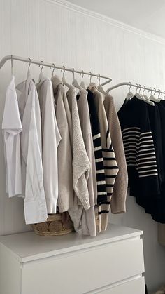 a white dresser topped with lots of sweaters hanging on it's hooks and clothes