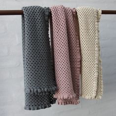 four crocheted scarves hanging on a clothes line with white brick wall in the background