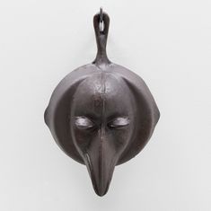 a metal mask hanging on the wall with eyes closed and one eye partially open, in front of a white background