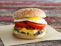 a hamburger with an egg, tomato and cheese on it sitting on top of a piece of paper