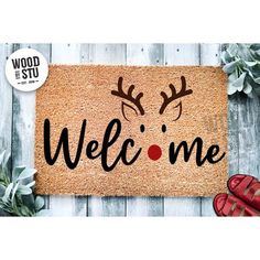 a door mat with the words welcome and reindeer antlers on it, next to red shoes