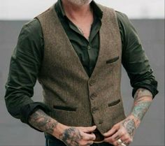 a man with tattoos on his arm wearing a brown vest and green shirt is looking at the camera