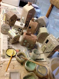 some clay houses are sitting on a table with paint and brushes in front of them