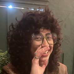 a woman with curly hair and glasses making a silly face in front of a mirror