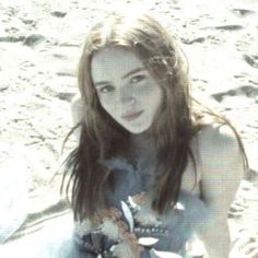 a woman sitting in the sand with flowers on her lap and looking at the camera