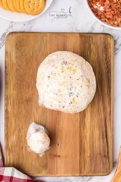 a cheese ball sitting on top of a wooden cutting board next to crackers and other food