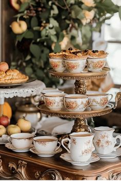 an assortment of tea cups and saucers on a table with apples in the background