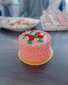 a pink cake sitting on top of a wooden table next to other plates and trays