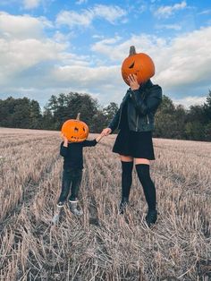 a woman and child holding hands with pumpkins on their heads in the middle of a field