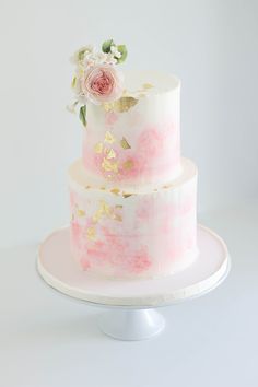 a three tiered cake with pink and white frosting on a plate, topped with flowers