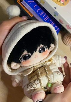 a hand holding a small doll with black hair and brown eyes, wearing a white hoodie