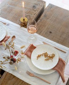 the table is set with two plates, silverware and some dried flowers on it