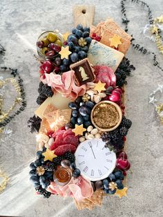 a clock surrounded by fruits, cheeses and crackers on a marble table top