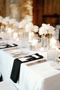 the table is set with white flowers and black napkins, silverware and candles