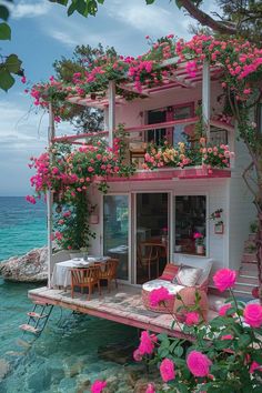 a house with pink flowers growing on the roof and balcony over looking the ocean in front of it