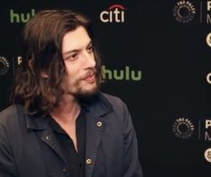 a man with long hair wearing a black shirt talking to someone on the red carpet