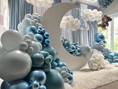 blue and white balloons are arranged in the shape of a crescent with a teddy bear on top