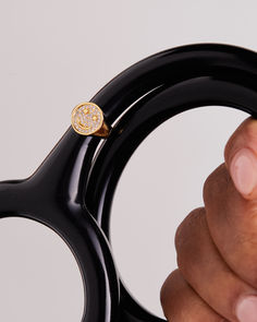 a hand holding a pair of black scissors with a gold ring on it's handle