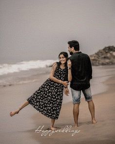 a man and woman standing on top of a beach next to the ocean holding hands