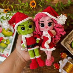 two crocheted dolls are being held by someone's hand on a table