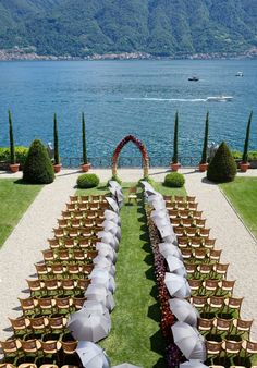 an outdoor ceremony set up with umbrellas and chairs on the grass by the water