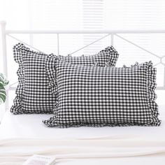 two black and white gingham pillows sitting on top of a bed next to a plant