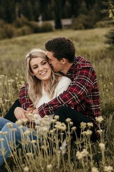 a man and woman are sitting in the grass with their arms around each other as they kiss