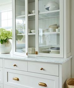 a white china cabinet with glass doors and gold handles in a kitchen or dining room