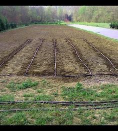 an empty field with trees in the background and barbed wire on the ground next to it