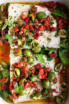 fish with tomatoes, brussel sprouts and herbs in a white casserole dish