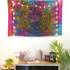 a tapestry hanging on the wall next to a potted plant and bookshelf