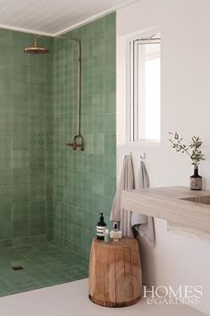 a green tiled bathroom with a wooden stool in front of the bathtub and shower