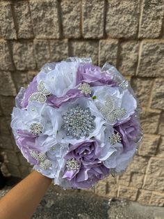 a bridal bouquet with purple and white flowers in front of a brick wall,