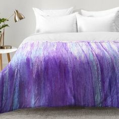 a bed with a purple and blue blanket on top of it next to a table