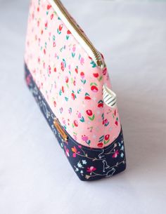 a pink and blue flowered purse with zippers on it sitting on a white surface