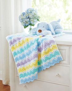 a blue teddy bear sitting on top of a dresser next to a crocheted blanket