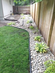 a garden with rocks and plants in the grass next to a wooden fenced area