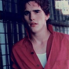 a young man in a red shirt leaning against a wall