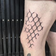 a man's leg with barbed wire tattoo on the side of his leg, next to a barbwire fence