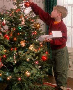 a young boy decorating a christmas tree with red, green and gold ornaments on it