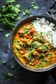 a bowl filled with rice and chicken curry next to cilantro on a table