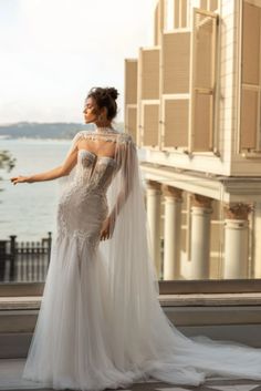 a woman in a wedding dress standing on a balcony looking out at the water and buildings