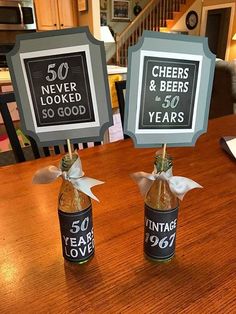 there are two beer bottles on the table with signs in them that say 50 years and cheers