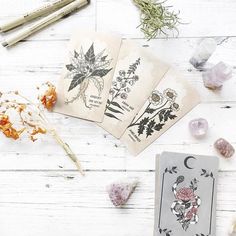 four cards with flowers on them sitting next to some crystals and pencils in front of them